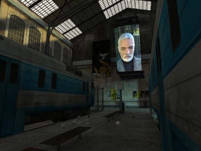 A screenshot from the video game Half-Life 2 showing an in-game environment with a dystopian train station, blue train carriage to the side, large video screen portraying a character known as Dr. Breen, and scattered debris on the platform.