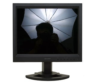 Silhouette of a person taking a photo with a camera, reflected in the screen of the Sharp LL-151-3D LCD Monitor, with a lighting umbrella visible in the reflection.