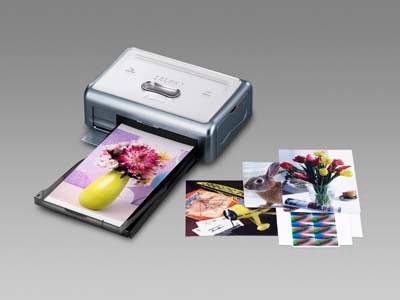 Canon Selphy CP500 compact photo printer with a sample of printed photos spread around it on a grey background.