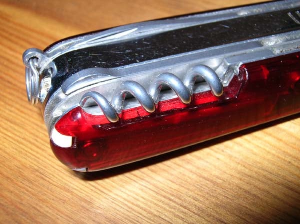 Close-up view of a Swiss Army knife showing the corkscrew tool on a wooden surface.