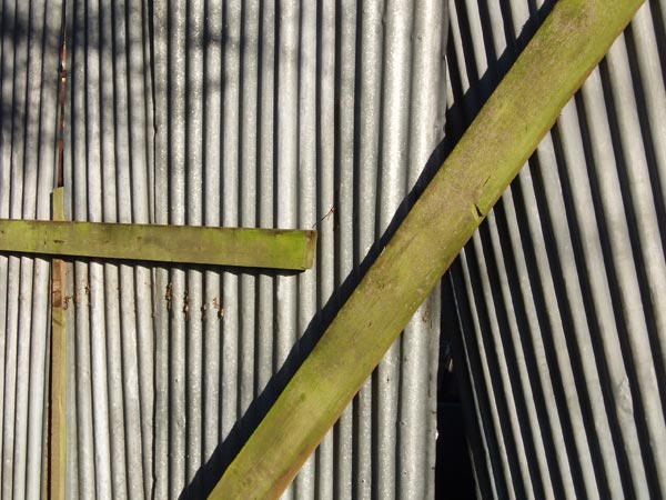 Close-up photo showing the texture and pattern of corrugated metal with a green wooden beam diagonally placed across it, taken with the Olympus µ (Mju) Digital 500 Digital Camera to demonstrate image quality and detail capture.