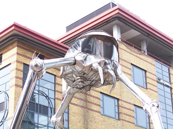 A metallic sculpture of a giant insect-like figure attached to the side of a modern building, showcasing sharp details and contrast captured by the Kodak EasyShare Z700 camera.