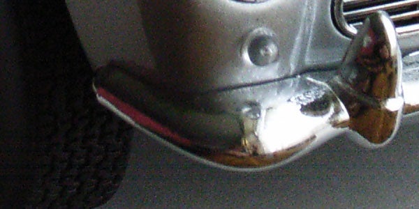 Close-up of a metallic object with a reflective surface, possibly part of the Ricoh Caplio R1V digital camera showing a distorted reflection.