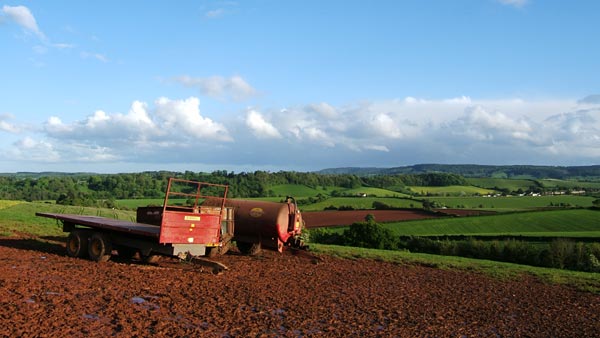 A scenic country landscape featuring green hills under a blue sky with clouds, with farm equipment in the foreground, possibly captured with the Fujifilm FinePix F810 Zoom camera.
