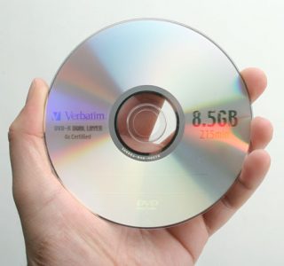 Hand holding a Verbatim double layer DVD disc with a storage capacity of 8.5GB, possibly related to a review of the NEC ND-3540A DVD Writer's capabilities.