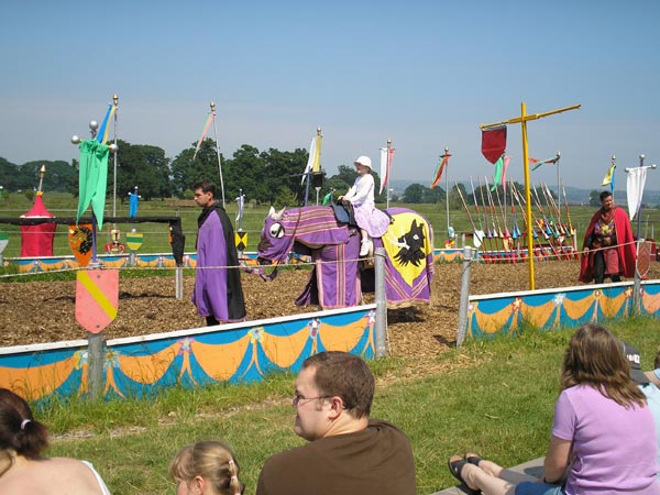 Young girl sitting on a colorful mechanical bull at an outdoor event, captured with the Olympus C-180 camera.A medieval-themed event with individuals in period costumes and colorful banners, as spectators watch from the foreground, taken with an Olympus C-180 camera.