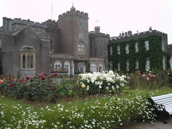 Photo taken with the Olympus C-180 camera featuring a historic castle surrounded by a vibrant garden with roses and a park bench in the foreground.