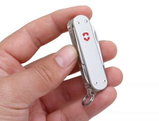 A hand holding the Swissbit SWISSMEMORY Victorinox retroALOX USB flash drive with Swiss Army knife design.