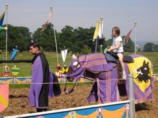 Outdoor event with child on a fake horse and person in cape.