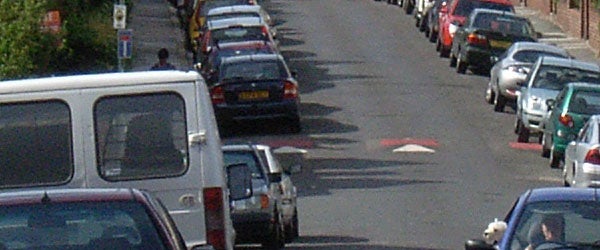 Photograph taken with the Ricoh Caplio GX8 digital camera showing a street view with parked cars on both sides.