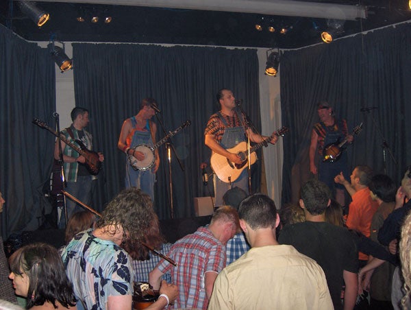 Photo taken with HP Photosmart R717 Digital Camera showing a live music performance with a band on stage and audience in the foreground, demonstrating the camera's low-light capabilities.