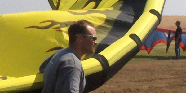 Image of a person with sunglasses standing in front of colorful kite-like structures on a clear day, taken with the HP Photosmart M22 Digital Camera.