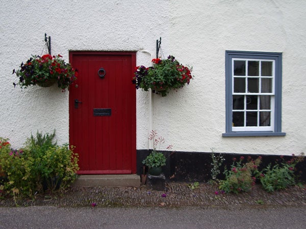 A quaint white cottage with a bright red door flanked by two hanging flower baskets, with a clear focus and accurate color representation indicative of image quality from the Pentax Optio S45 digital camera.