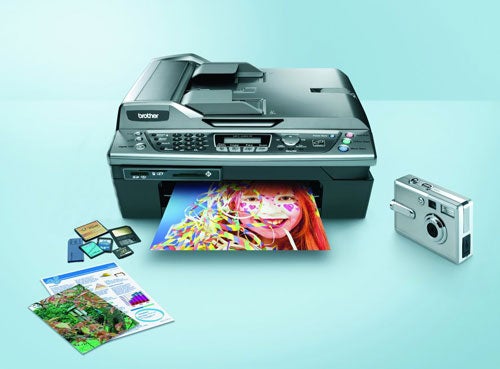 Brother MFC-620CN multifunction printer with printed sample images, SD cards, and a camera on a blue surface.
