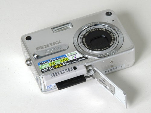 Pentax Optio S5z digital camera displayed open with its battery compartment visible on a light background.