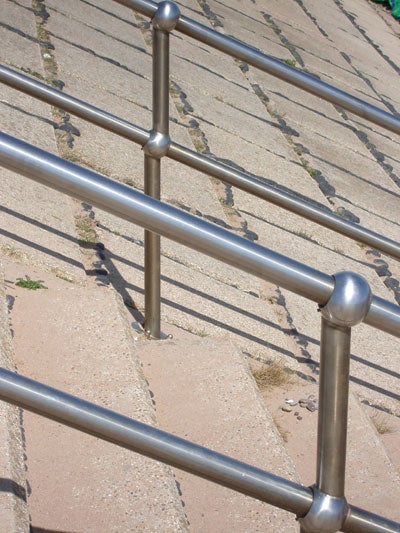 Photo taken with Pentax Optio S5z showing a close-up of shiny metal railings on a stone stairway, demonstrating the camera's detail and color capture in daylight.