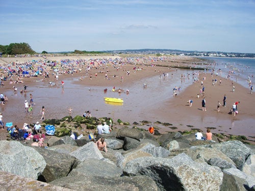 A busy beach scene with numerous people enjoying the sun and wading into the water, taken with a Pentax Optio S5z camera.