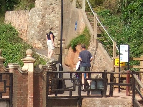 Photograph taken with a Fujifilm Z1 camera showing a slightly blurry scene of two people at the bottom of some outdoor stairs, with a woman ascending the stairs to the left and a stone wall in the background.