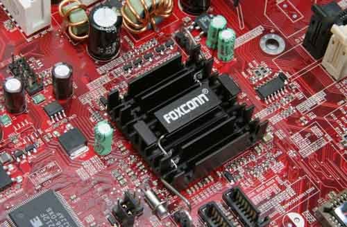 Close-up view of a Foxconn 955X7AA-8EKRS2 Motherboard showcasing its red PCB, capacitors, CPU socket, and heatsink with the Foxconn logo visible.