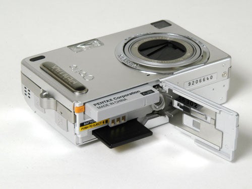 A Pentax Optio SVi digital camera with the battery compartment open, displaying the battery and memory card slots on a white background.