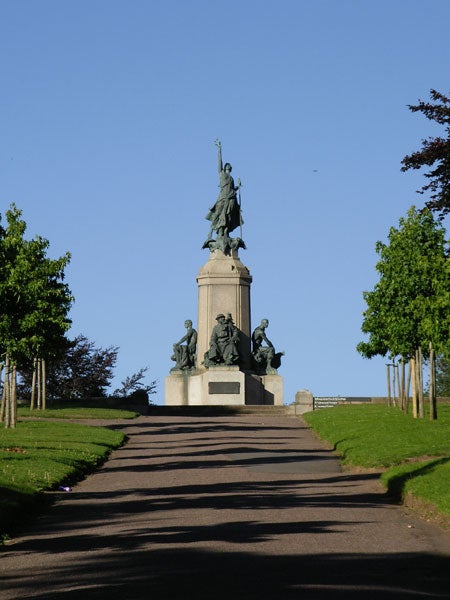 Photo taken with a Pentax Optio SVi digital camera, showcasing a monument statue at the top of a staircase flanked by green trees under a clear blue sky.