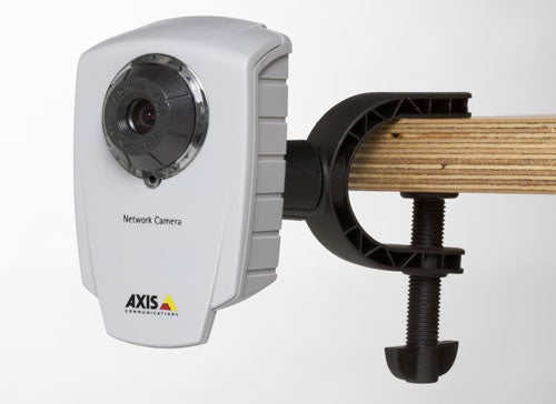 Axis Communications 207 Network Camera mounted on a wooden surface with a black clamp, featuring a white housing and the AXIS logo on the front.