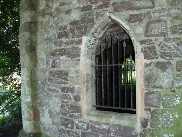 A photograph of an ancient stone wall with a gothic arched window secured by iron bars, possibly taken with an Olympus µ [mju] Digital 800 camera, demonstrating the camera's color reproduction and detail in daylight conditions.