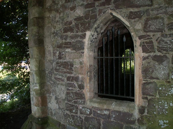 A photo showing a detailed view of an old stone building with a pointed arched window secured with metal bars, suggesting an image taken by Konica Minolta Dimage X1 as an example of its photograph quality.