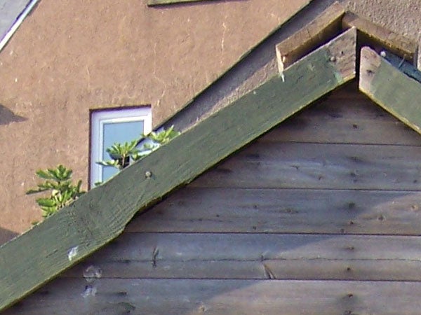 Photograph showing the detail and zoom capability of the Kodak Easyshare V550 camera featuring a close-up view of a building's roof, with evident detail of the wooden shingles and a window in the background.