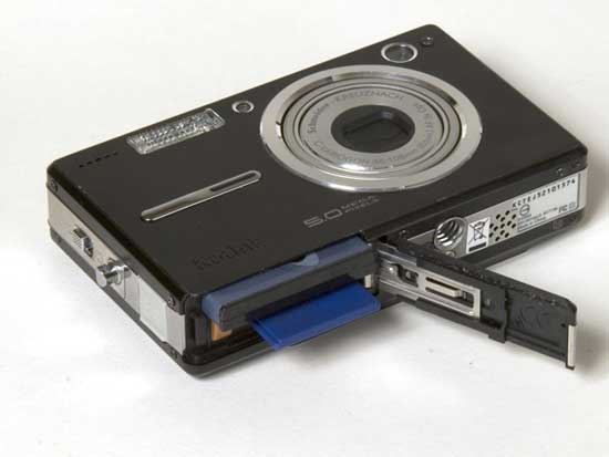 Kodak Easyshare V550 digital camera with built-in lens and battery compartment open, showing USB cable and SD card slot.