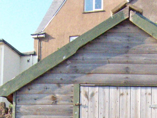 A photograph taken with the Kodak Easyshare V550 camera showcasing the camera's zoom capability, featuring a close-up of a wooden shed and house roof under a clear sky.