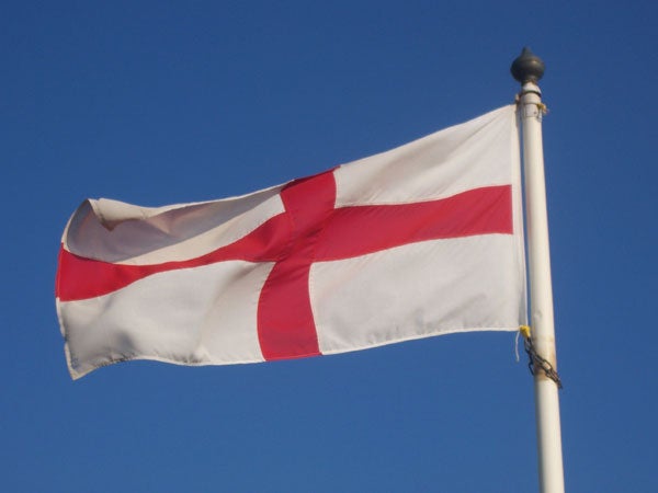 White flag with a red cross on a blue sky background displayed on a flagpole.