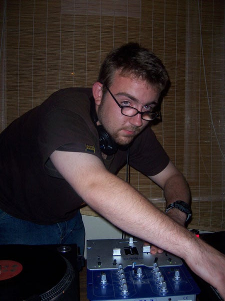 Man adjusting equipment while DJing with a vinyl turntable and audio mixer.
