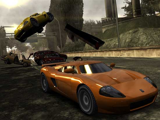 Screenshot from the video game Burnout: Revenge showing an orange sports car racing on a street with several other cars involved in a crash, including one airborne yellow car and debris flying.