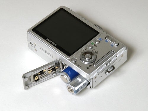 Pentax Optio S55 digital camera with open battery compartment displaying two AA batteries.