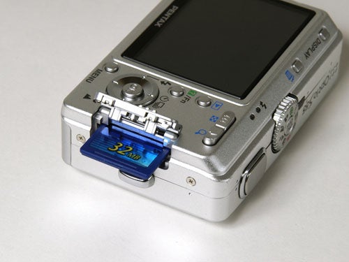 Pentax Optio S55 digital camera with an open memory card slot displaying a 32MB SD card.