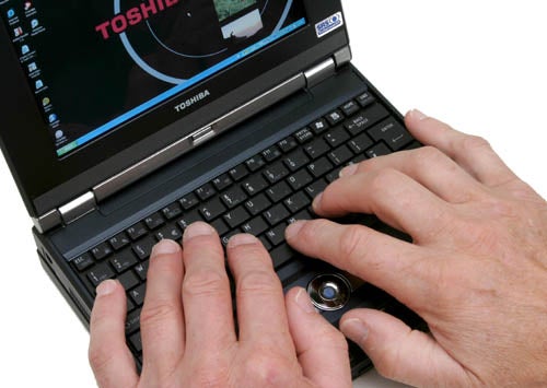 Hands typing on the keyboard of a Toshiba Libretto U100 mini notebook computer.