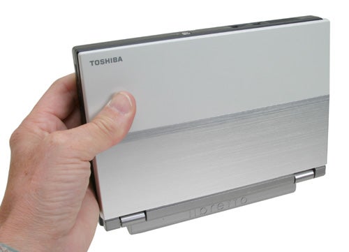 A hand holding a closed Toshiba Libretto U100 mini-notebook, showing the exterior design with the Toshiba logo visible.