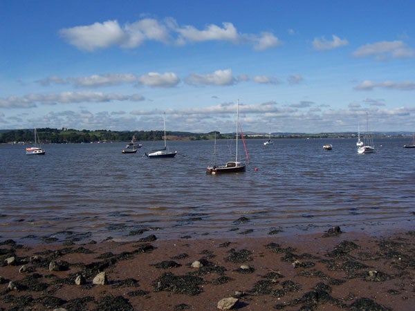 A clear photograph of a calm lakescape capturing several boats anchored on water with a rocky shoreline in the foreground, under a partly cloudy sky, potentially taken with a Kodak EasyShare C360 camera.
