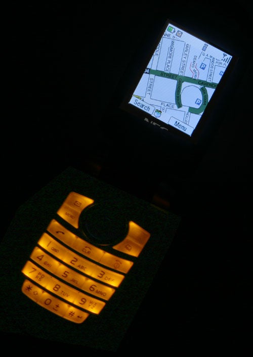 NEC N411i i-mode phone showing a lit screen with map application in a dark environment, keypad glowing in orange light.