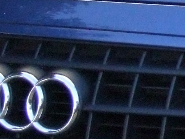 Close-up photo of the Audi logo and grille, likely taken with a camera with a high zoom feature such as the Fujifilm FinePix S9500. The image is slightly out of focus, indicating motion blur or low light performance.