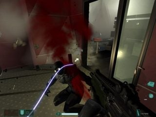 In-game screenshot from F.E.A.R. showing a first-person perspective where the player is firing a weapon at an enemy character in an office environment, with bullet impact and blood splatter effects visible.