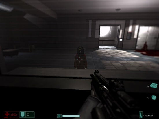 Screenshot from the video game F.E.A.R. First Encounter Assault Recon showing a first-person view of the player character holding a rifle with a red dot sight aimed down a corridor with blood splatter on the wall and floor.