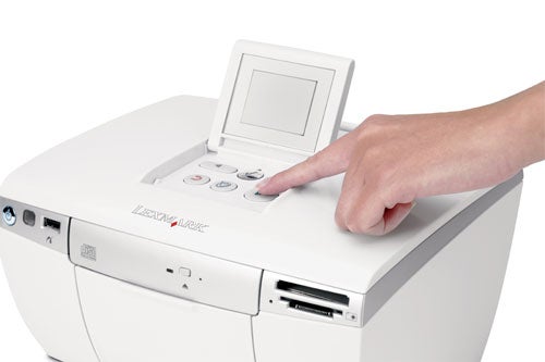 A person's hand pressing a button on the Lexmark P450 Photo Printer with an LCD screen displayed.
