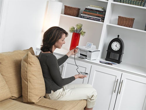 Woman sitting on a couch and printing a photo using a Lexmark P450 Photo Printer located on a white cabinet in a home setting.