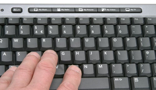 Close-up of a person using the Microsoft Media Center 2005 Keyboard, highlighting multimedia keys like My Music, My Radio, My Pictures, and My Videos above the function keys.