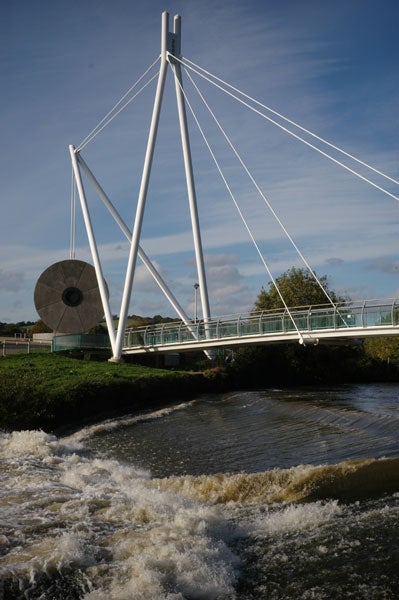 Photograph taken with an Epson R-D1 digital rangefinder camera depicting a modern pedestrian bridge with white suspension cables over a river with rushing water.