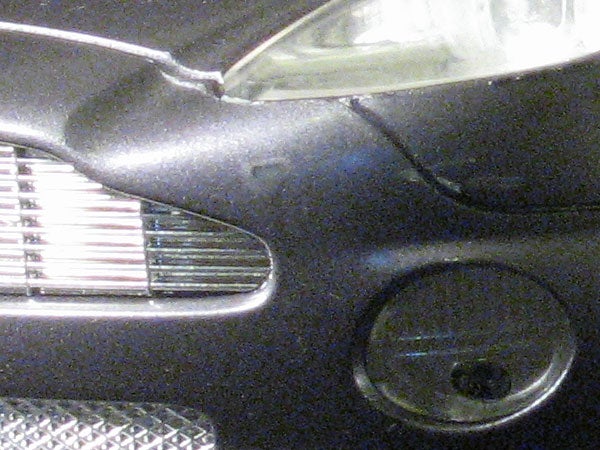 Close-up of a black car's front left side, showing part of the headlight, grille, and fog light.
