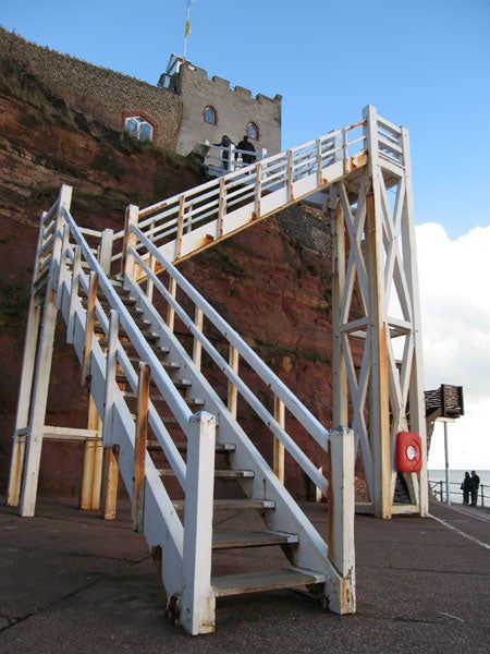 White wooden staircase leading to a lookout point at a seaside cliff with a blue sky in the background.