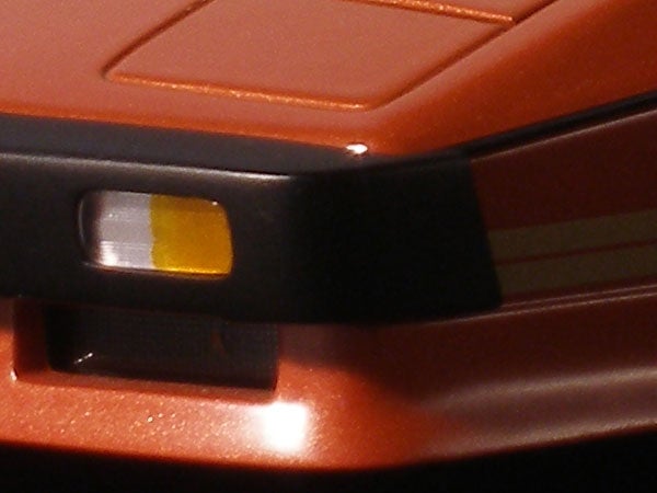 Close-up image of the Olympus SP-350 digital camera showing a part of the orange metallic body and a black grip with the shutter button and a control interface detail visible.